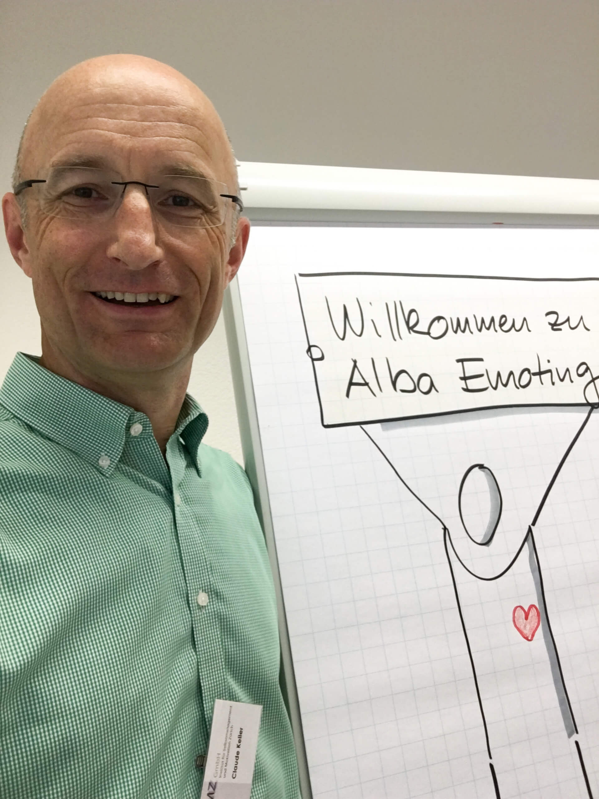 Selfie von Claude Keller mit Flipchart auf dem "Willkommen zu Alba Emoting" steht.