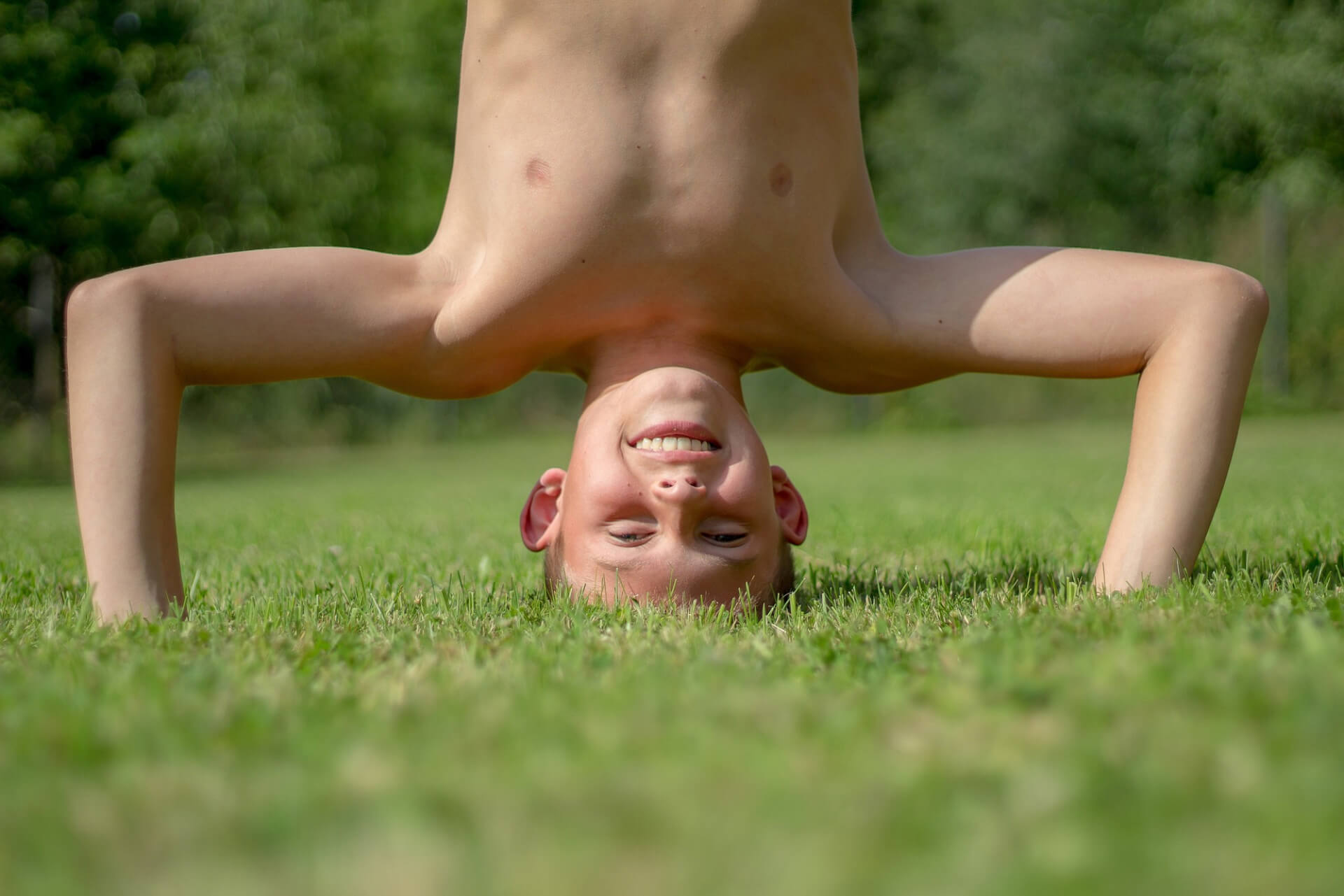 Ein kleiner Junge macht einen Handstand im Gras.