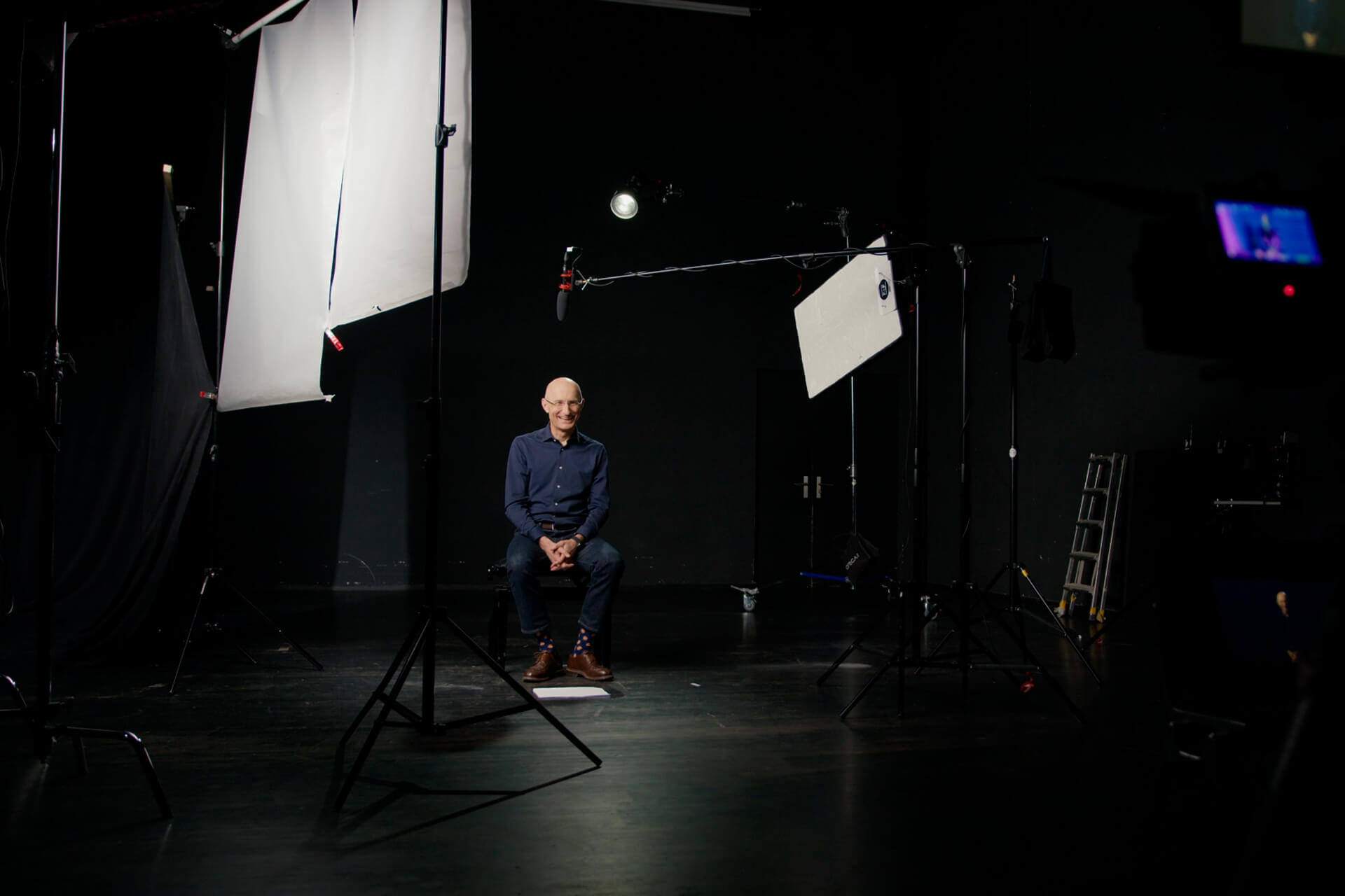 Claude Keller sitzt vor einer Kamera in einem dunklen Raum.